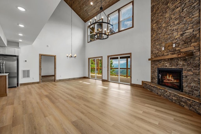 unfurnished living room featuring wooden ceiling, a high ceiling, an inviting chandelier, a stone fireplace, and light hardwood / wood-style flooring