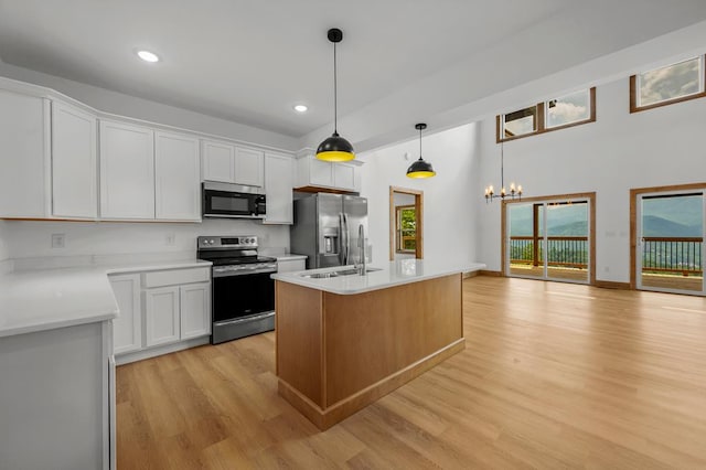 kitchen featuring appliances with stainless steel finishes, a center island with sink, white cabinetry, and hanging light fixtures