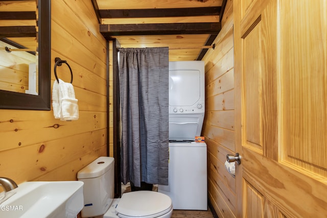 bathroom with beamed ceiling, stacked washer / dryer, and wooden walls