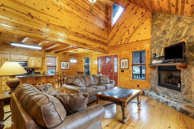 living room with wood walls, wooden ceiling, a high ceiling, a stone fireplace, and light wood-type flooring