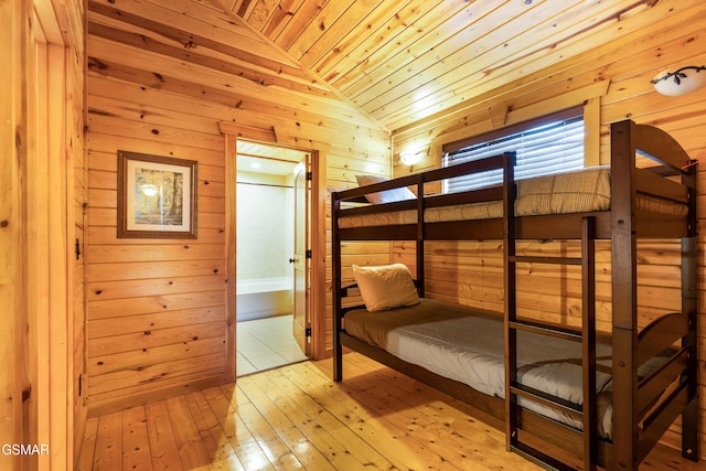 unfurnished bedroom with light wood-type flooring, ensuite bath, wood ceiling, vaulted ceiling, and wood walls