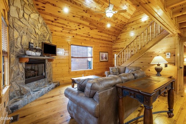 living room with wood walls, a stone fireplace, light hardwood / wood-style flooring, ceiling fan, and wood ceiling