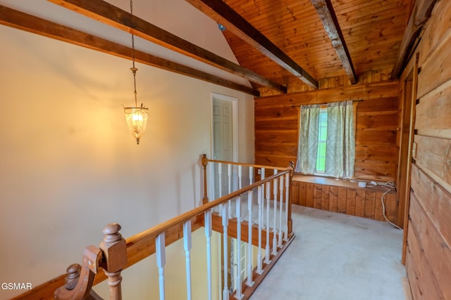 hall with an upstairs landing, wood ceiling, wood walls, carpet flooring, and beam ceiling