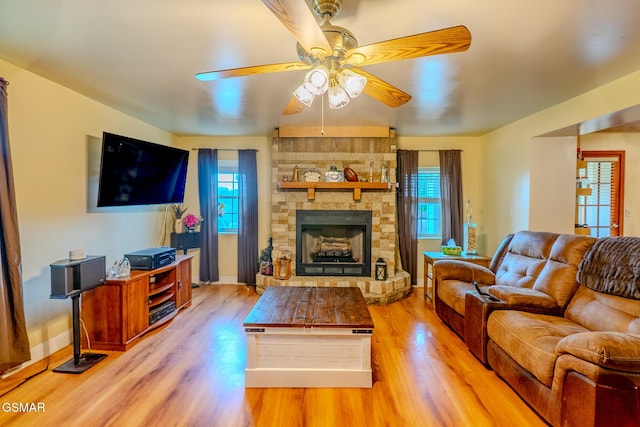 living room featuring a stone fireplace, a ceiling fan, wood finished floors, and plenty of natural light
