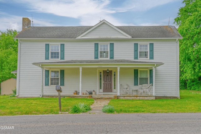 view of front of home with a front yard, roof with shingles, a chimney, and covered porch
