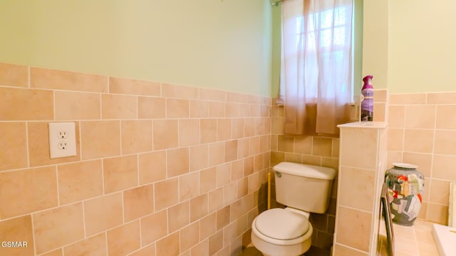 bathroom featuring tile walls, toilet, and a wainscoted wall