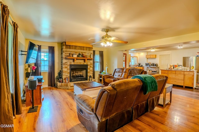 living area with ceiling fan, a fireplace, and light wood-style flooring