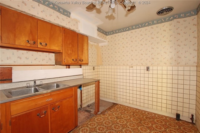 kitchen featuring dark tile patterned flooring, tile walls, and sink