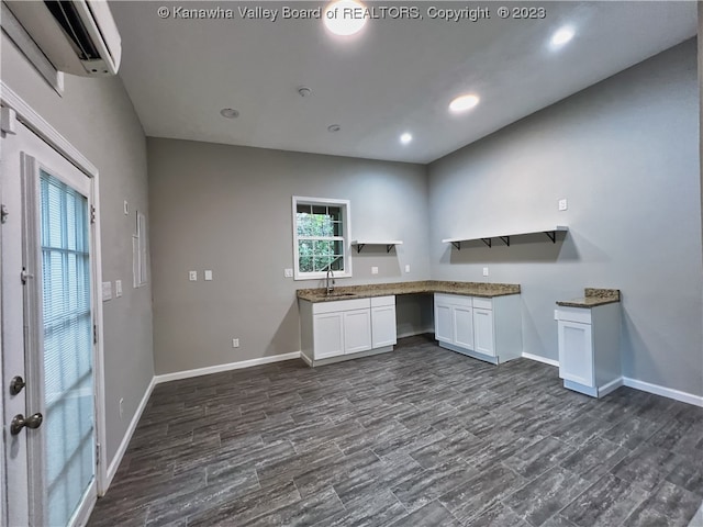 kitchen featuring stone countertops, sink, white cabinets, and an AC wall unit