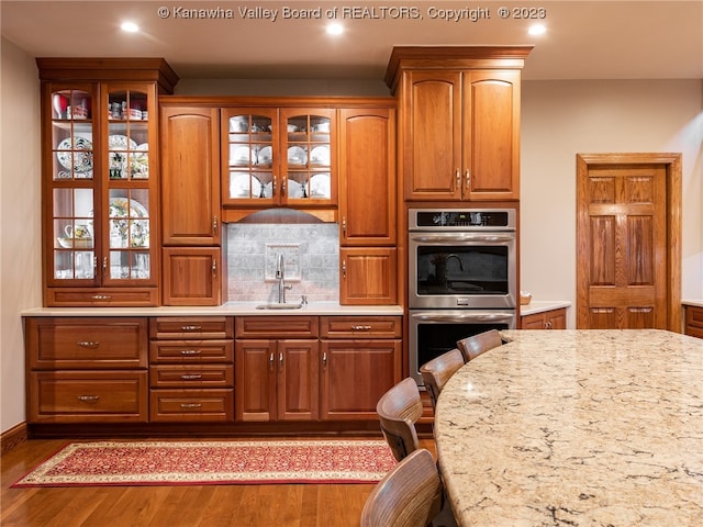 kitchen with sink, tasteful backsplash, wood-type flooring, and double oven