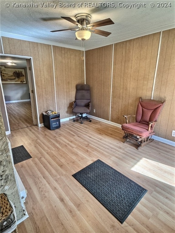 sitting room with wood walls, a textured ceiling, ceiling fan, and light wood-type flooring