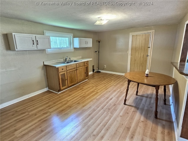 kitchen featuring white cabinets, a textured ceiling, light hardwood / wood-style floors, and sink