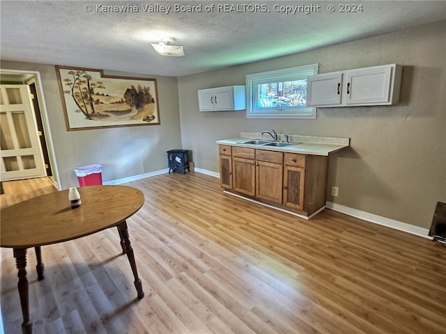 kitchen with white cabinets, light hardwood / wood-style floors, a textured ceiling, and sink