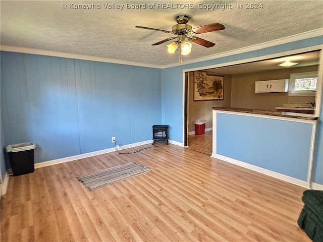 unfurnished room featuring ceiling fan, a wood stove, crown molding, a textured ceiling, and light wood-type flooring