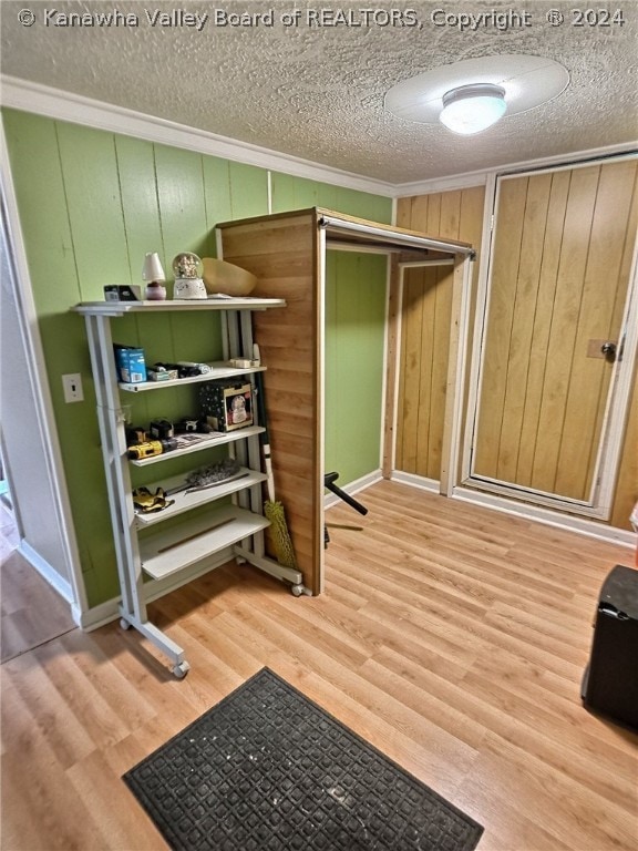 workout room with wood walls, a textured ceiling, light hardwood / wood-style floors, and ornamental molding