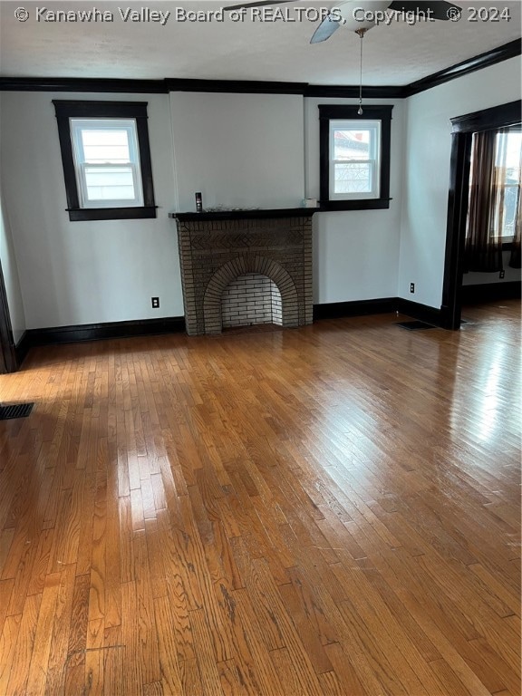 unfurnished living room featuring ceiling fan, a brick fireplace, dark wood-type flooring, and crown molding