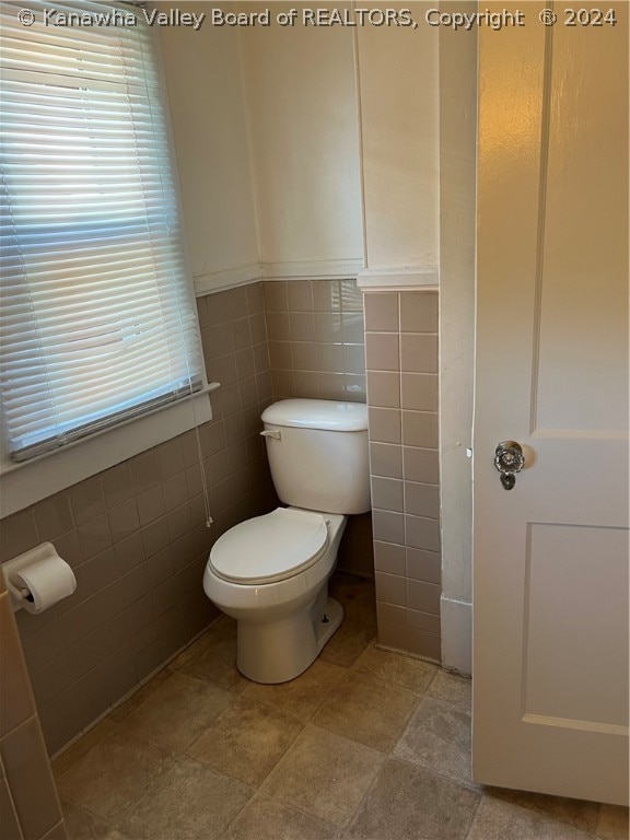 bathroom with tile flooring, tile walls, and toilet