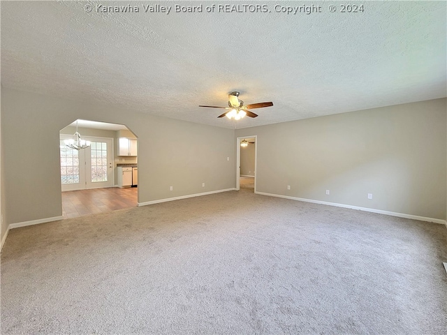 spare room featuring ceiling fan with notable chandelier, carpet floors, and a textured ceiling