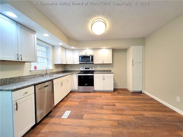 kitchen with sink, stainless steel appliances, dark hardwood / wood-style floors, a textured ceiling, and white cabinets