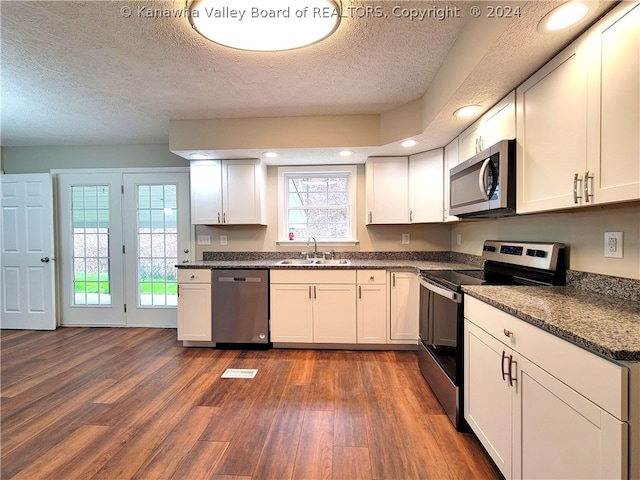 kitchen featuring appliances with stainless steel finishes, white cabinetry, sink, dark stone counters, and dark wood-type flooring