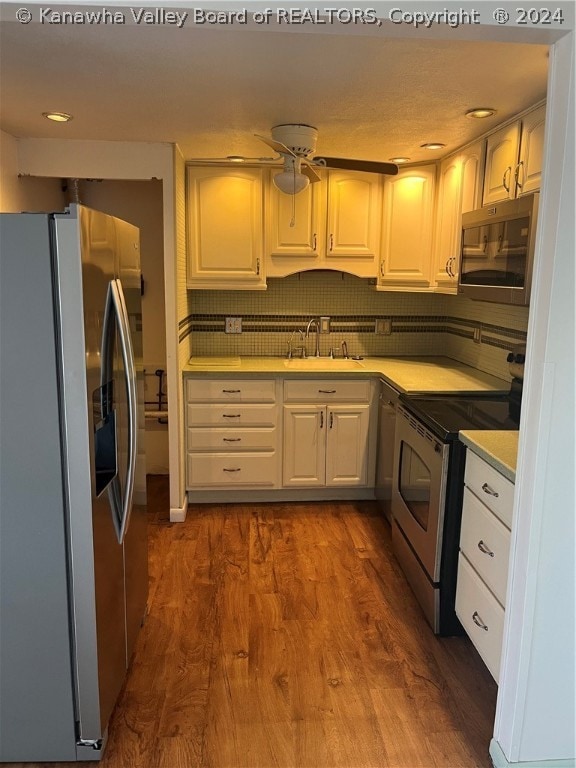 kitchen with appliances with stainless steel finishes, backsplash, dark hardwood / wood-style floors, white cabinetry, and sink