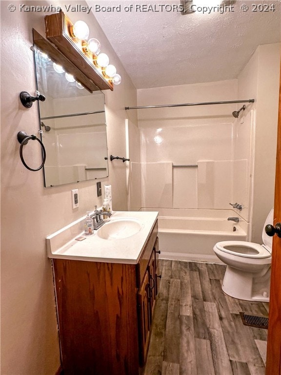 full bathroom featuring a textured ceiling, hardwood / wood-style floors, shower / washtub combination, toilet, and vanity