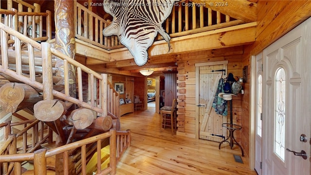 entrance foyer featuring wood walls, a towering ceiling, and light hardwood / wood-style floors