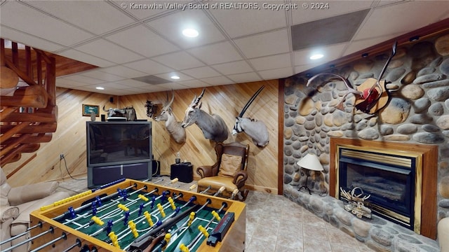 playroom with a stone fireplace, wood walls, and a drop ceiling