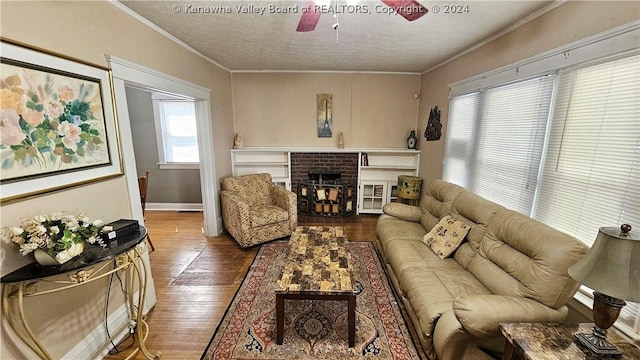 living room featuring ceiling fan, a brick fireplace, crown molding, wood-type flooring, and a textured ceiling