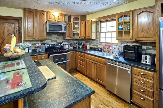 kitchen with decorative backsplash, appliances with stainless steel finishes, sink, and light hardwood / wood-style flooring