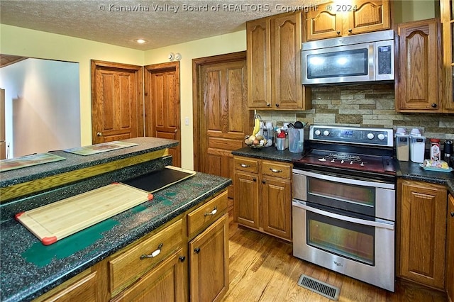 kitchen featuring appliances with stainless steel finishes, dark stone countertops, light hardwood / wood-style floors, a textured ceiling, and decorative backsplash