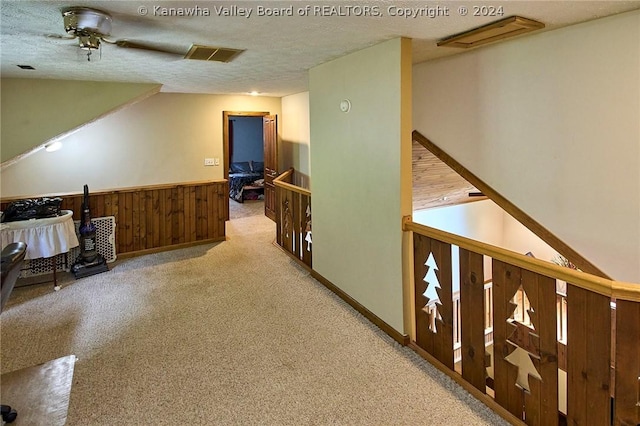 hall featuring light carpet, a textured ceiling, and wood walls