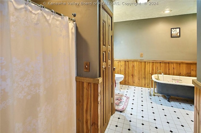 bathroom with toilet, wooden walls, a textured ceiling, and a washtub