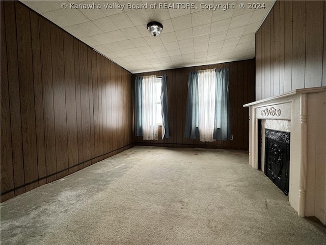 unfurnished living room with a fireplace, light colored carpet, and wooden walls