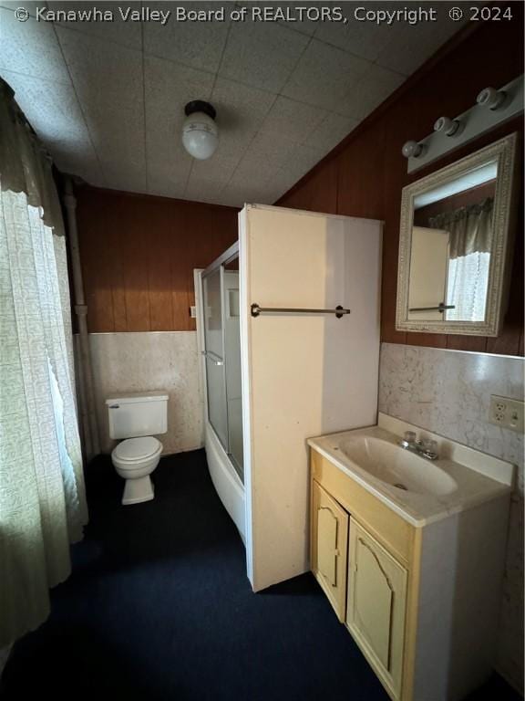 full bathroom with combined bath / shower with glass door, vanity, toilet, and wooden walls