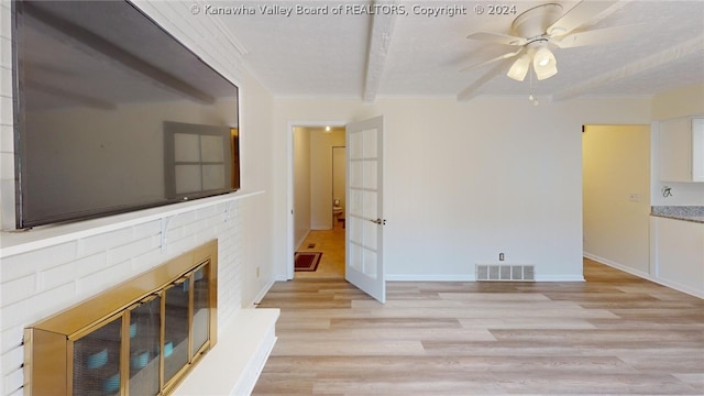 unfurnished living room featuring a fireplace, beam ceiling, light hardwood / wood-style flooring, and ceiling fan