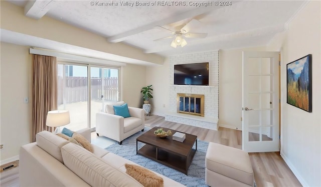 living room with a brick fireplace, a textured ceiling, ceiling fan, light hardwood / wood-style flooring, and beamed ceiling