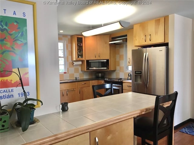 kitchen featuring stainless steel appliances, tile countertops, hardwood / wood-style floors, and wall chimney range hood