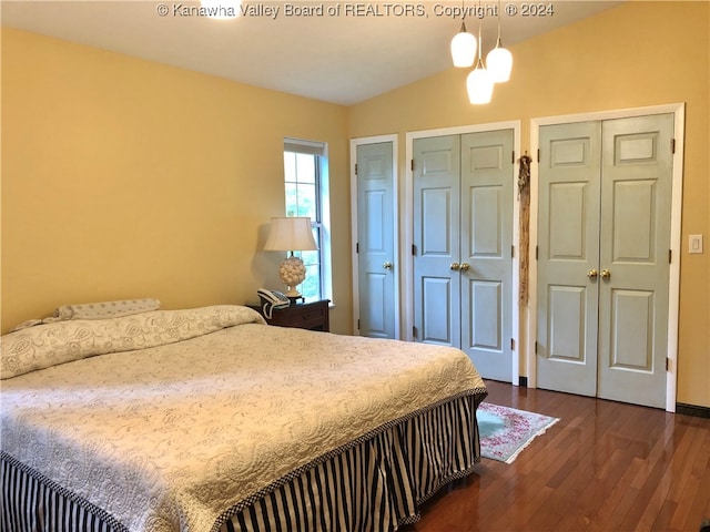 bedroom featuring two closets, an inviting chandelier, wood-type flooring, and lofted ceiling