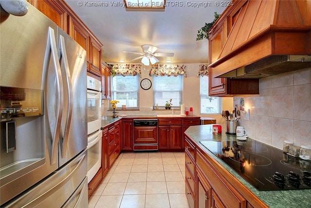 kitchen with custom exhaust hood, stainless steel fridge, a wealth of natural light, black electric stovetop, and white oven