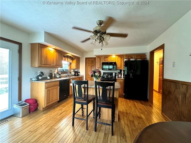 kitchen with a breakfast bar, ceiling fan, light hardwood / wood-style floors, black appliances, and a kitchen island