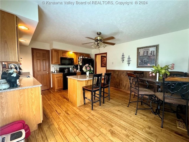 kitchen featuring light hardwood / wood-style flooring, a textured ceiling, a kitchen breakfast bar, and black appliances