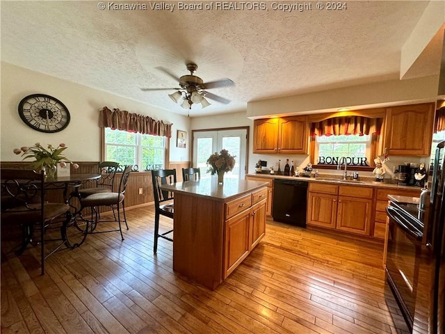 kitchen with sink, a center island, ceiling fan, black appliances, and light wood-type flooring