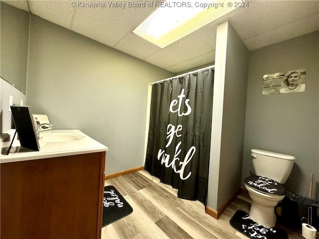 bathroom with walk in shower, toilet, wood-type flooring, vanity, and a drop ceiling