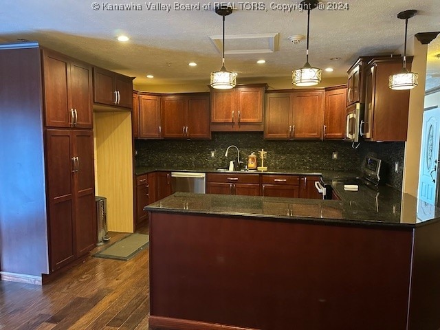 kitchen featuring dark stone counters, stainless steel appliances, hanging light fixtures, decorative backsplash, and dark wood-type flooring