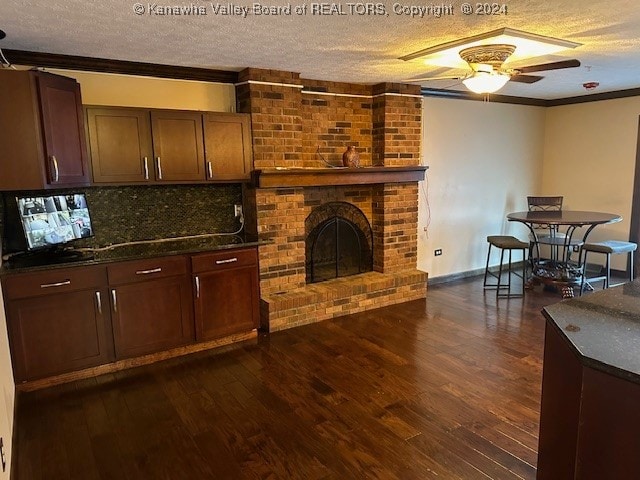 kitchen featuring dark wood-type flooring, ornamental molding, ceiling fan, and a brick fireplace