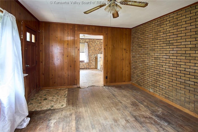 spare room featuring ceiling fan, hardwood / wood-style flooring, a healthy amount of sunlight, brick wall, and wood walls