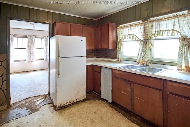 kitchen featuring light countertops, freestanding refrigerator, a sink, wooden walls, and dishwasher