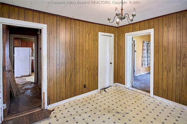 spare room featuring a notable chandelier, baseboards, and wooden walls