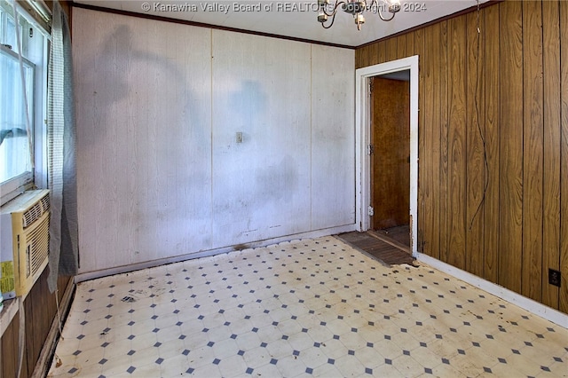 empty room featuring wooden walls, ornamental molding, light tile patterned floors, and an inviting chandelier